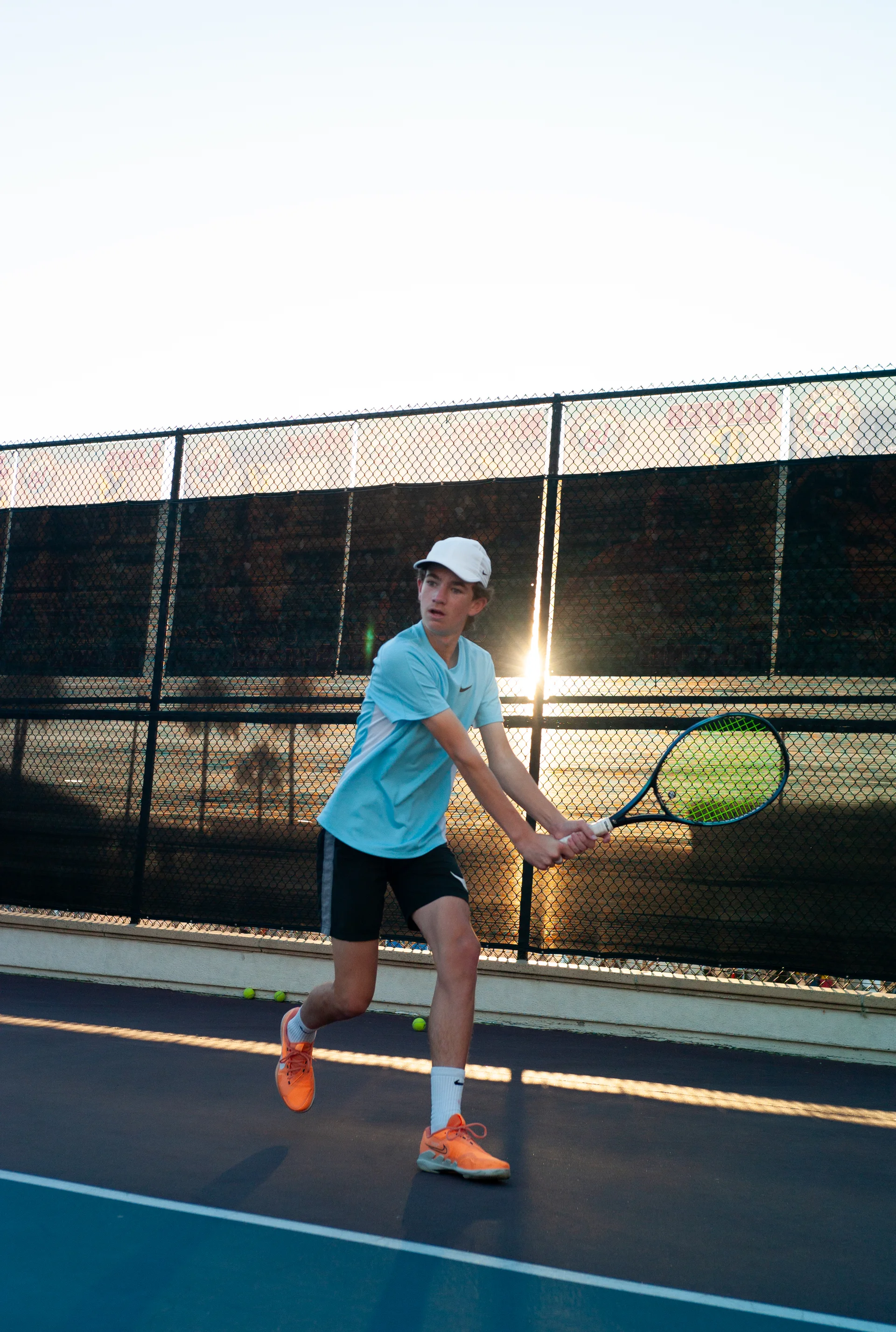 A junior driving a two-handed backhand on court at golden hour