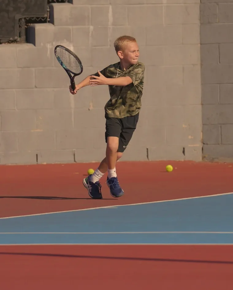 A junior player driving through a groundstroke during training