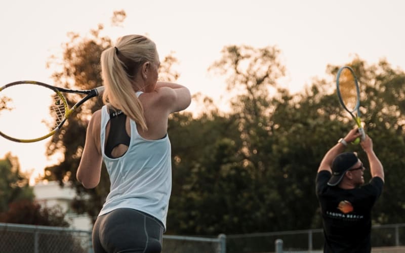 An adult following through on a swing with a coach demonstrating alongside her
