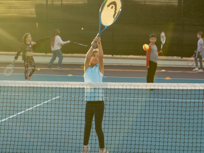 Kids rallying at the net during Orange Ball session in golden-hour light